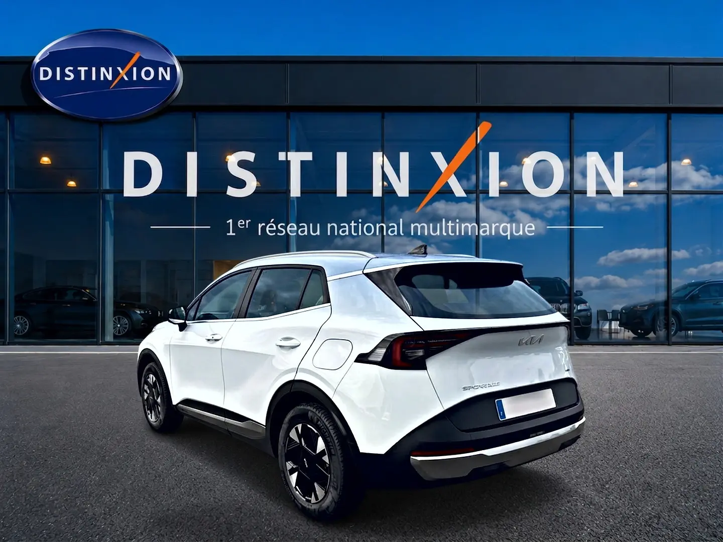 Vue 3/4 arrière droite d'un KIA SPORTAGE blanc 2026 avec jantes alu noires devant un showroom Distinxion.