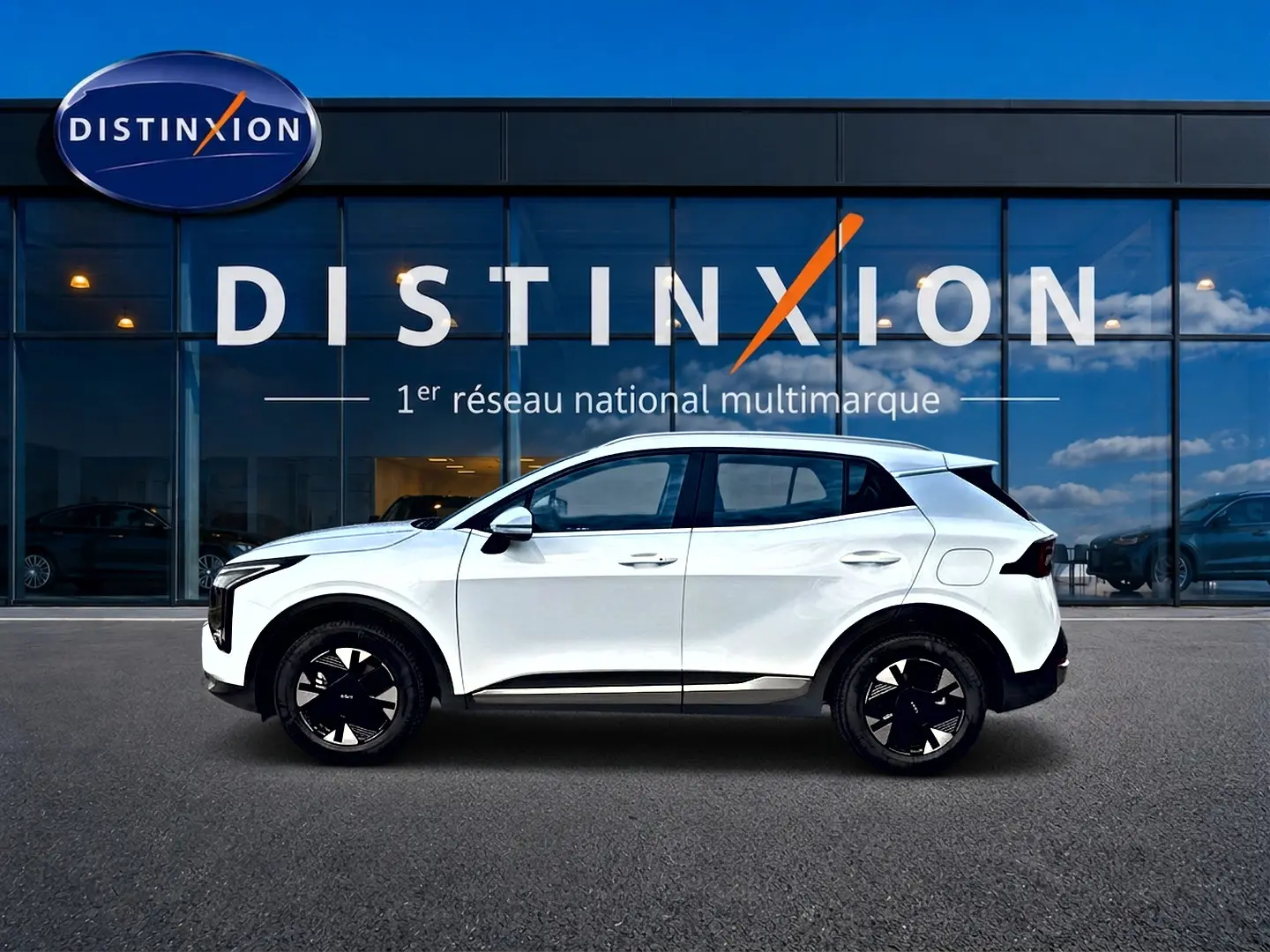 Vue de profil côté gauche d'un KIA SPORTAGE blanc 1.6 hybride 239 active avec jantes alu noires devant une vitrine Distinxion.