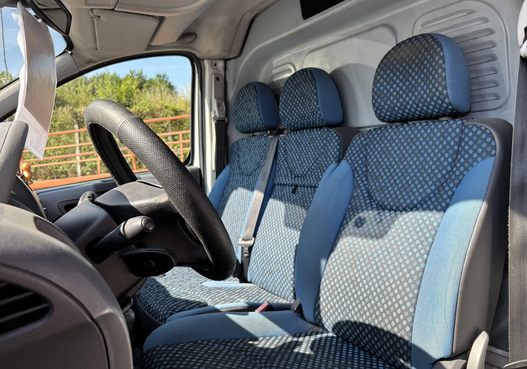 Vue intérieure côté conducteur du FIAT Scudo Fourgon blanc, montrant les sièges bleus à motifs et le volant noir.
