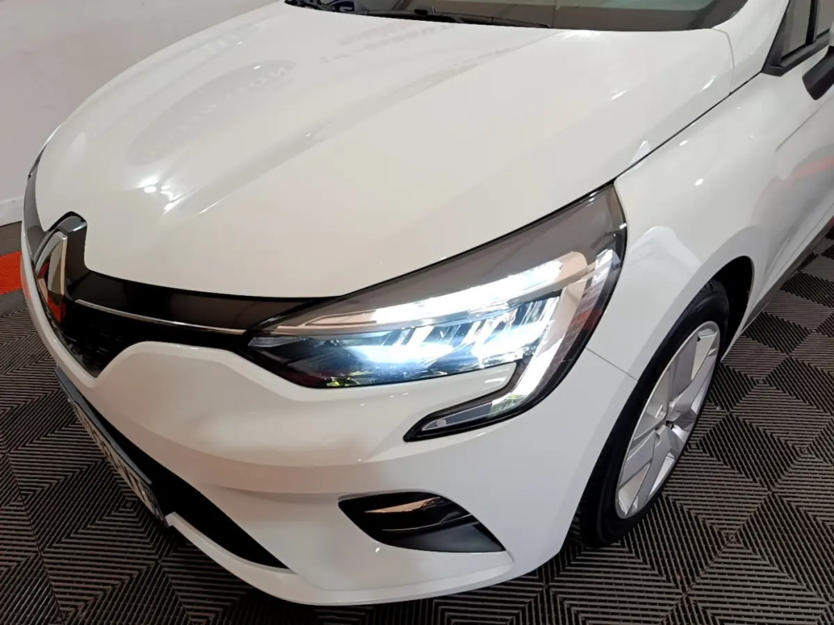 Vue 3/4 avant droit d'une Renault Clio Business blanche avec phares LED allumés et jantes modernes.