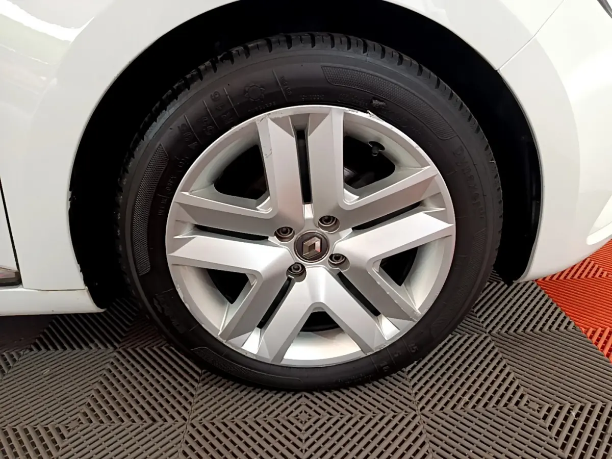 Gros plan sur la roue avant gauche d'une Renault Clio Business blanche, jante alliage à cinq branches doubles.