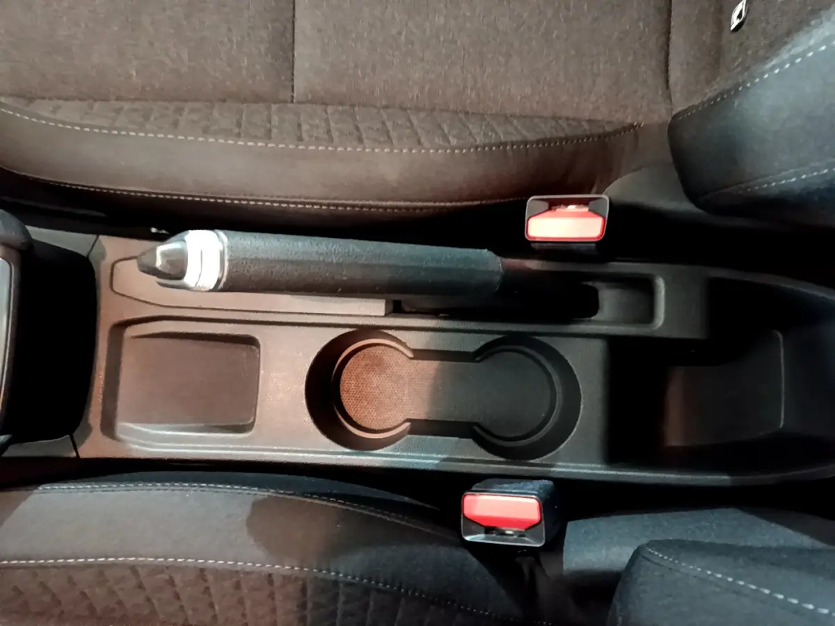 Vue plongeante sur la console centrale noire avec frein à main et porte-gobelets entre les sièges avant d'une Renault Clio blanche.