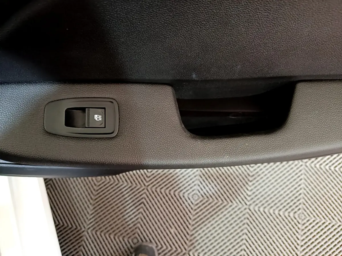 Détail de la commande de lève-vitre sur la porte intérieure noire d'une Renault Clio Business blanche de 2021.