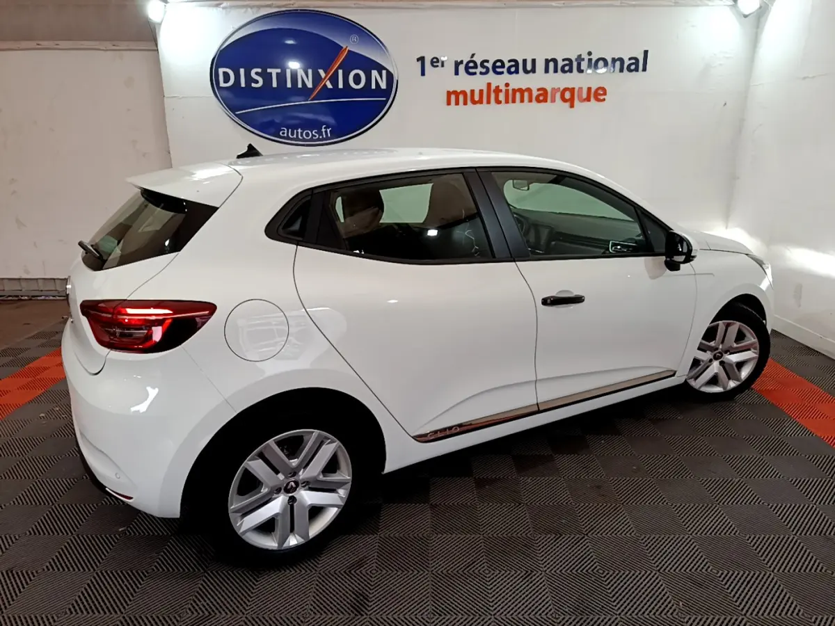 Renault Clio Business blanc vue 3/4 arrière côté droit, feux arrière allumés et jantes alliage visibles.