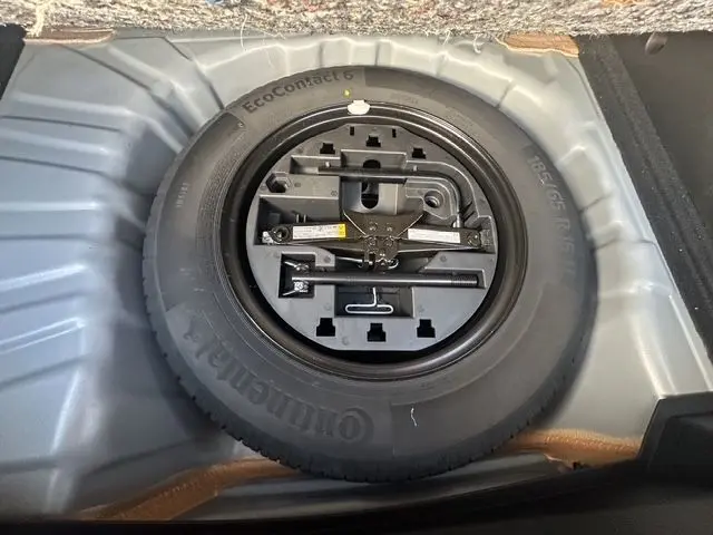 Gros plan sur la roue de secours et ses outils dans le compartiment de coffre d'une Renault Clio V gris Highland.