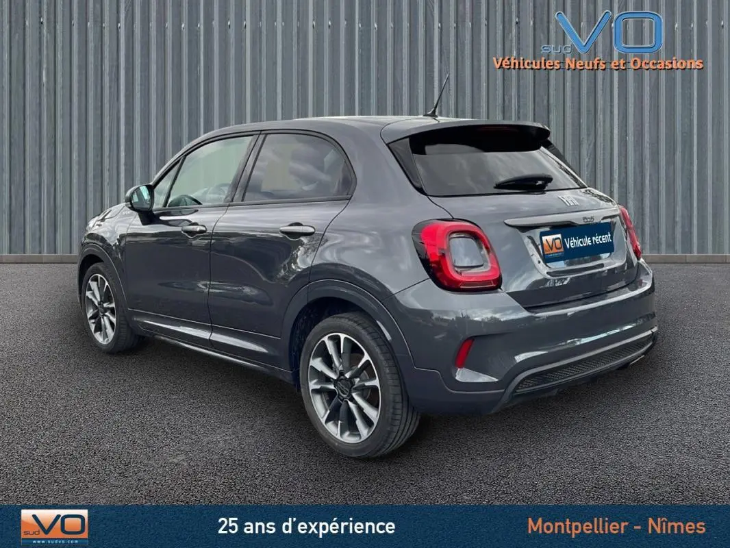 Vue 3/4 arrière droite d'une FIAT 500X gris métallisé avec jantes alliage 18 pouces sur fond urbain.