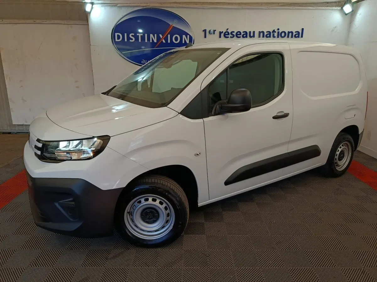 Vue 3/4 avant droit d’un Peugeot Partner blanc 2026 avec pare-chocs noir et jantes acier en intérieur showroom.