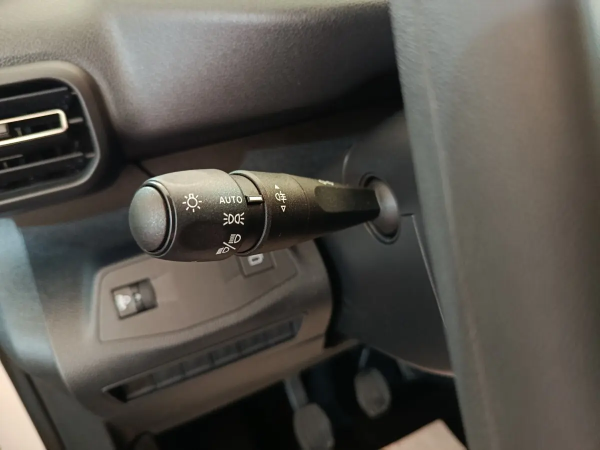 Gros plan sur la commande des phares à gauche du volant dans l'habitacle noir du Peugeot Partner blanc.