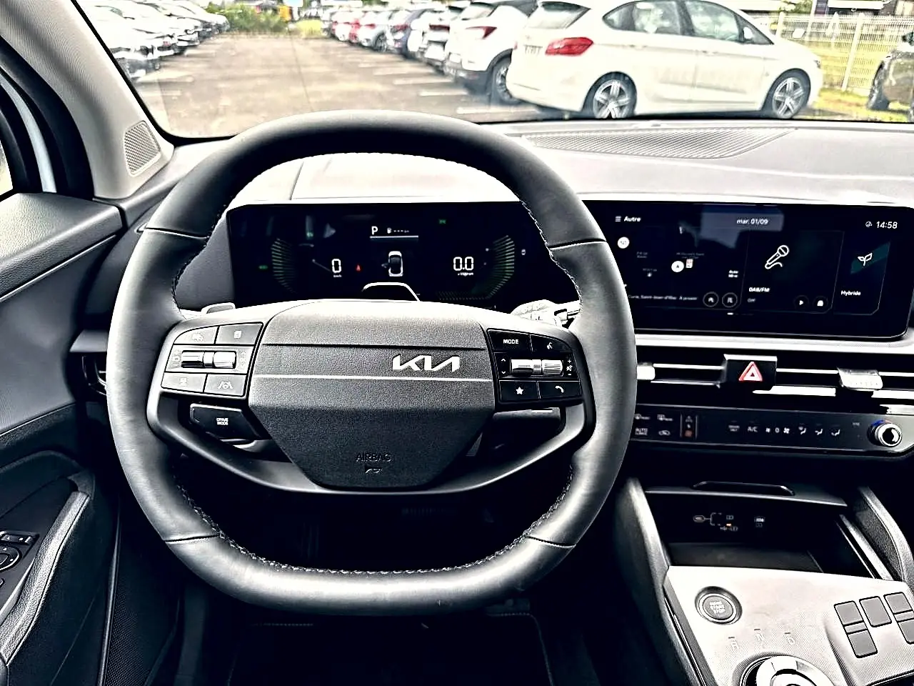 Vue intérieure centrée sur le volant cuir noir et le tableau de bord numérique du Kia Sportage blanc 2026 hybride.