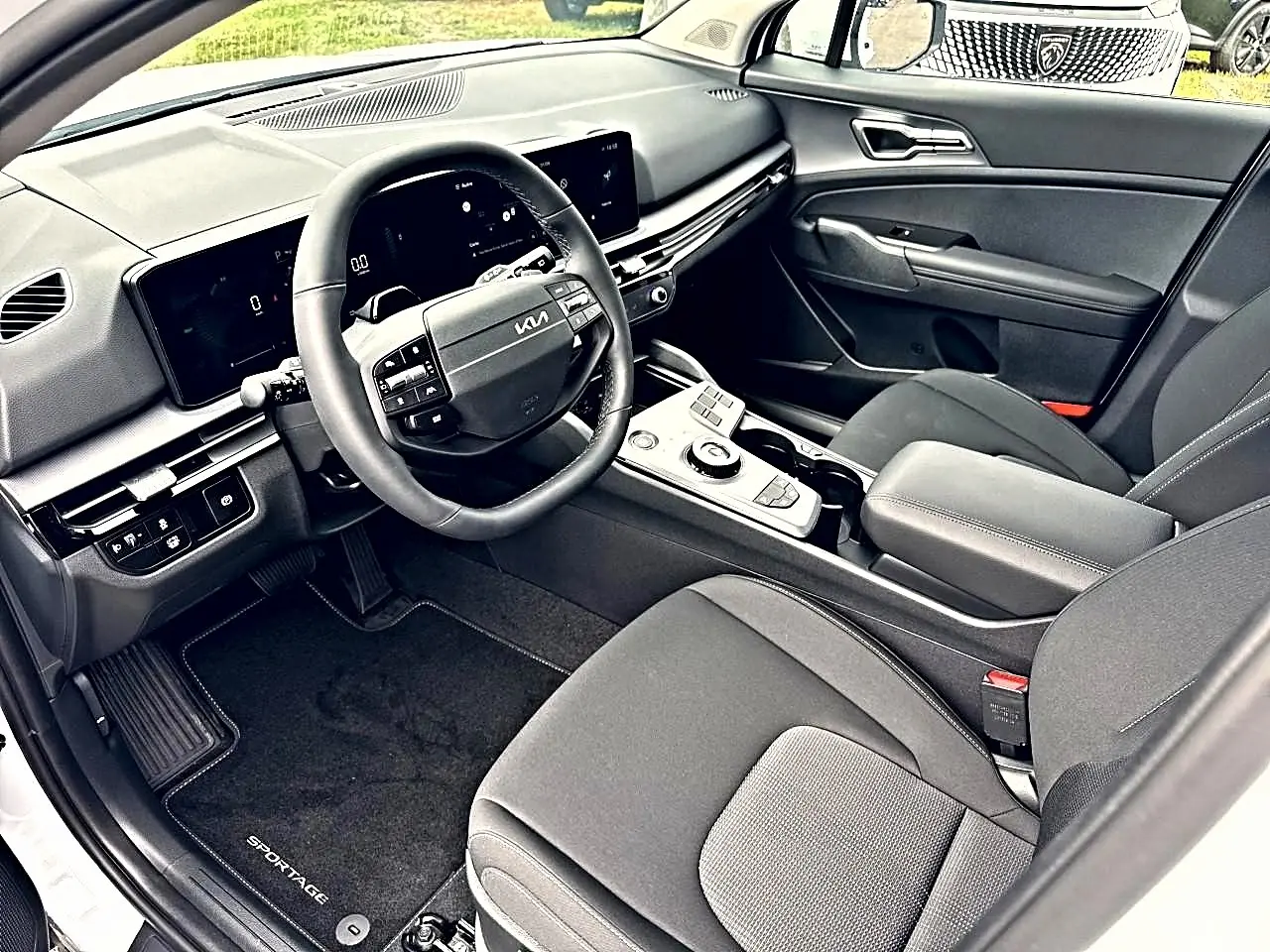 Vue intérieure côté conducteur du Kia Sportage 2026 hybride, montrant le volant cuir multifonction et la console centrale moderne.