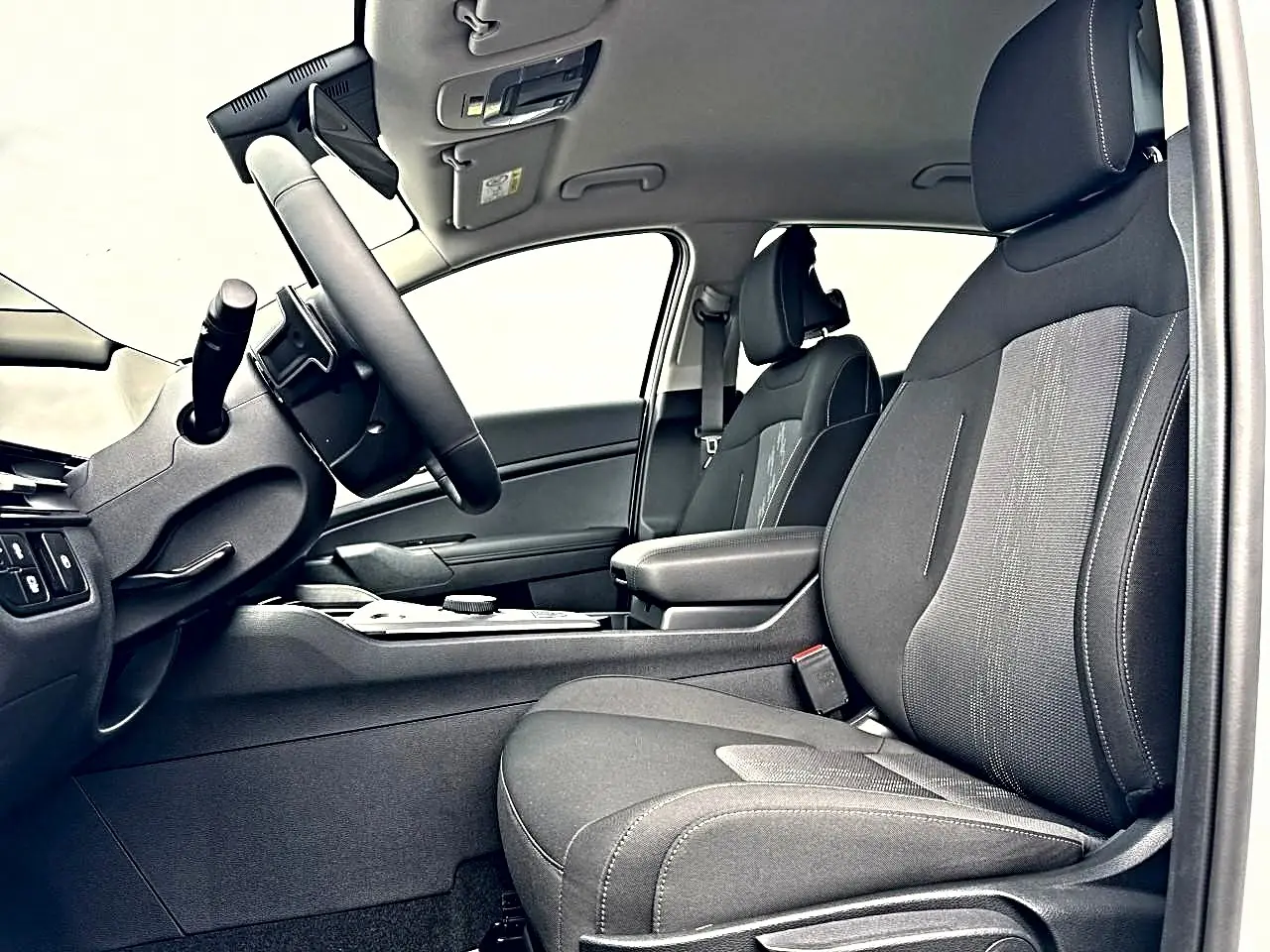 Intérieur côté conducteur du Kia Sportage 1.6 hybride 2026, sièges noirs avec accoudoir central et volant multifonction.