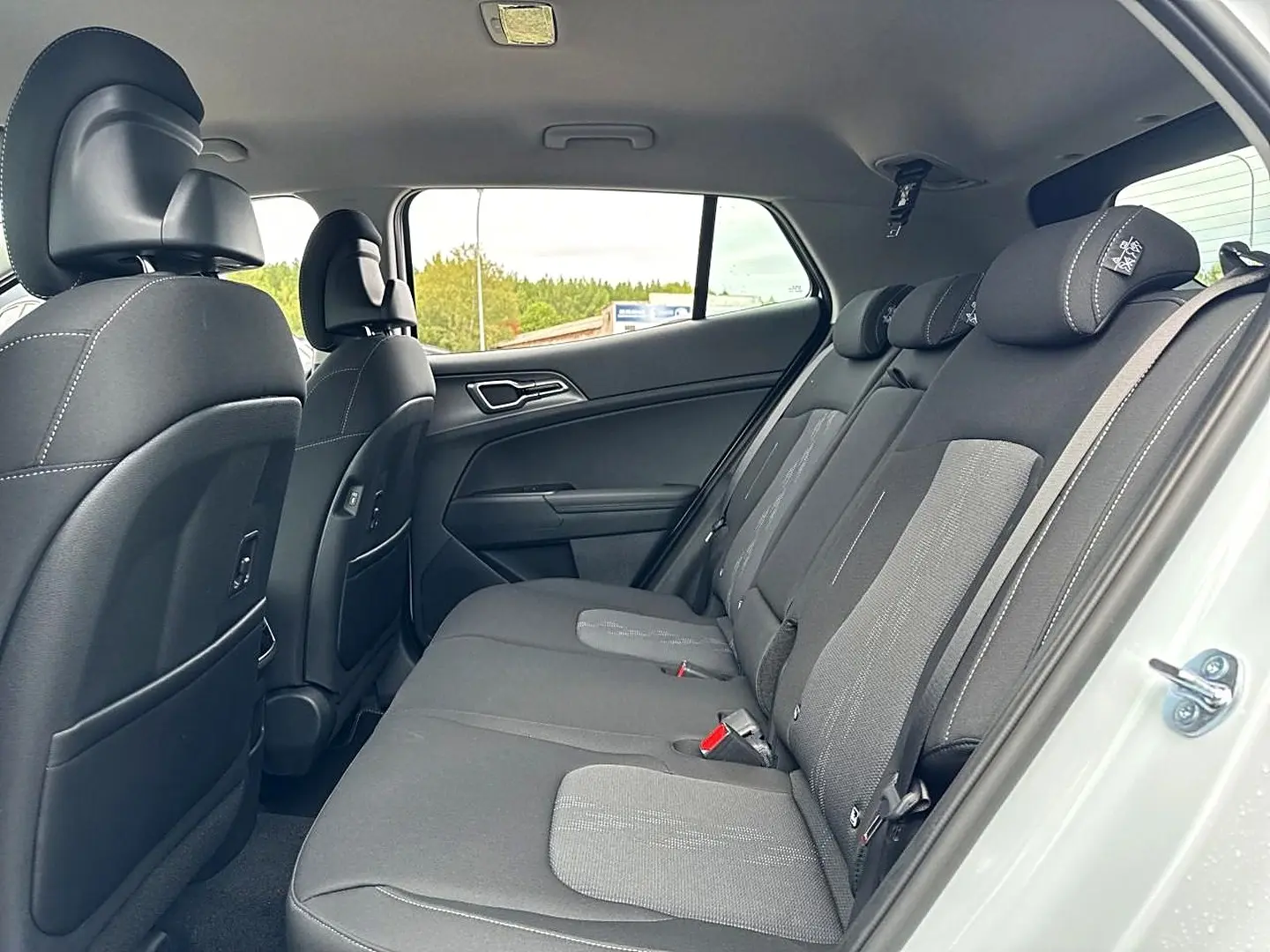 Vue intérieure côté droit montrant la banquette arrière grise et noire du Kia Sportage 1.6 hybride blanc 2026.