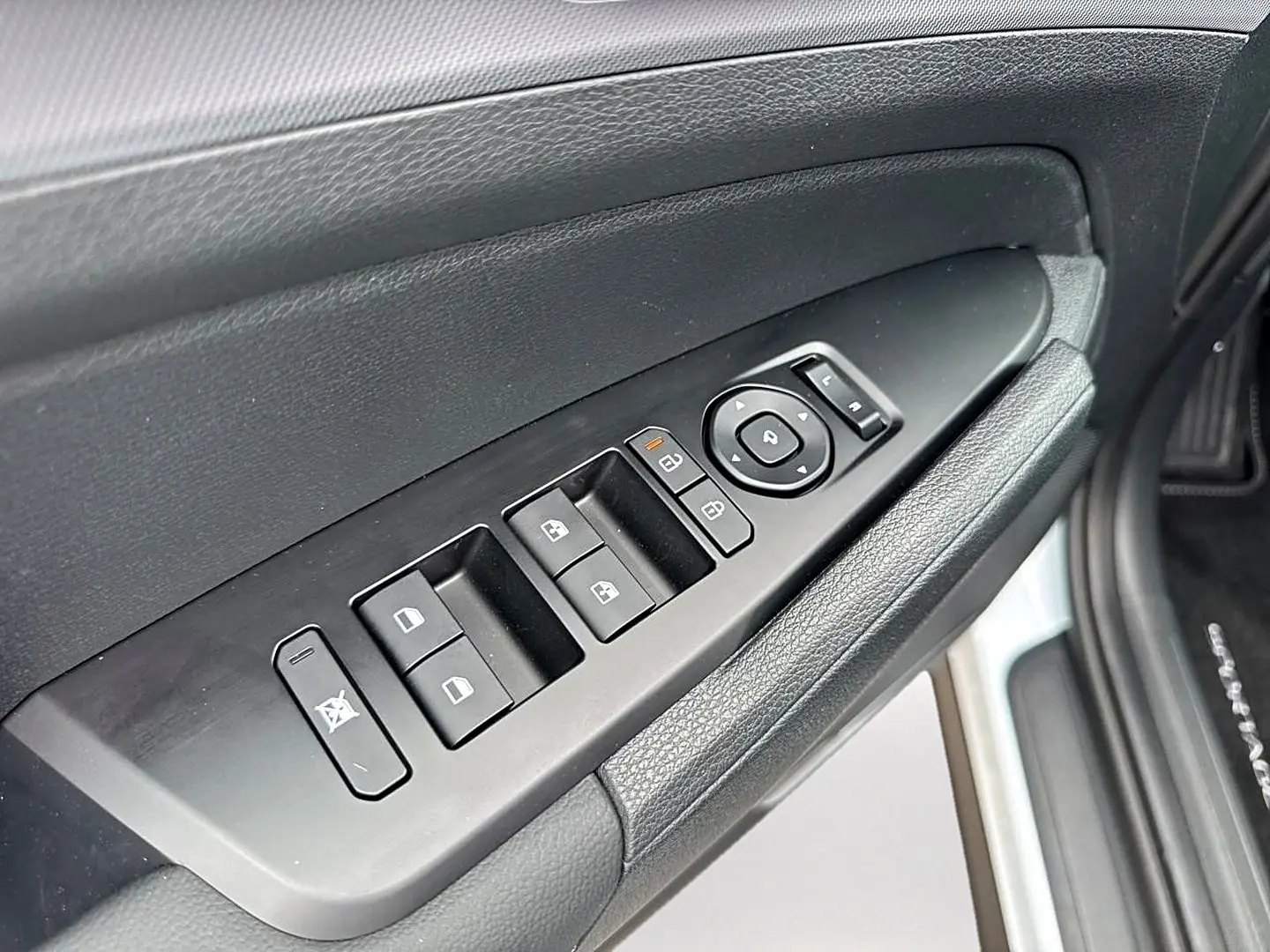Gros plan sur la commande des vitres et rétroviseurs côté conducteur du Kia Sportage blanc, avec texture cuir noire.