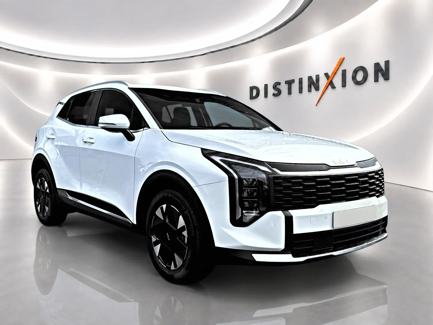Vue 3/4 avant gauche d'un Kia Sportage blanc 2026 avec calandre noire et jantes alu noires en showroom.