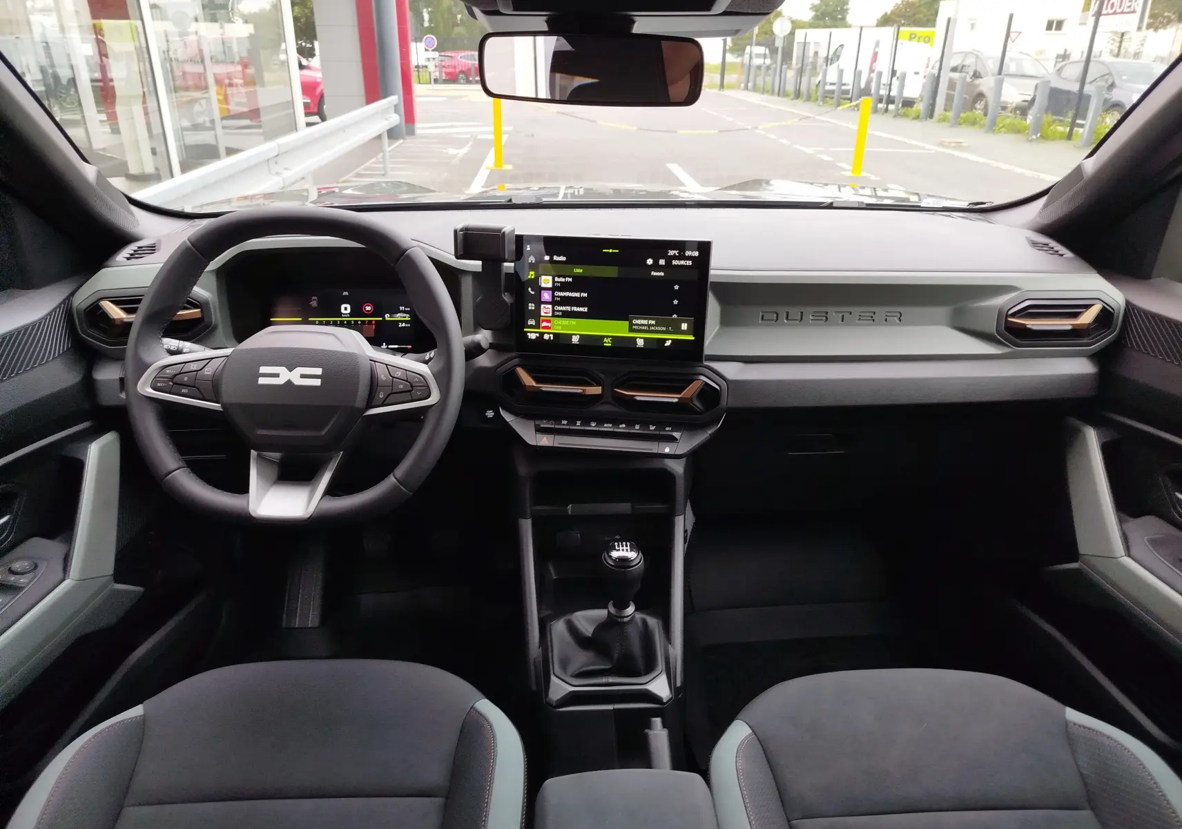 Vue intérieure frontale du tableau de bord du Dacia Duster 2025 avec écran tactile, volant multifonction et levier de vitesse manuel.