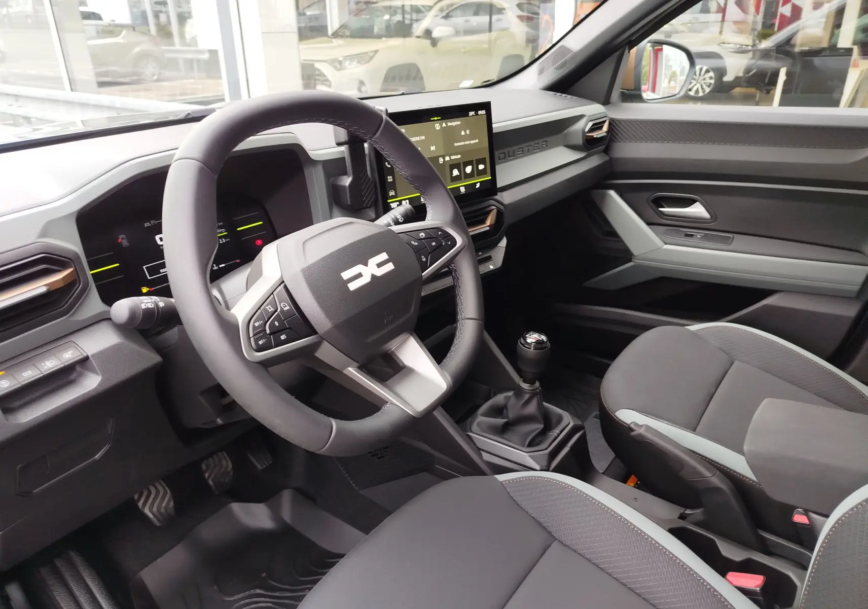 Vue intérieure côté conducteur du Dacia Duster 2025, tableau de bord moderne avec écran tactile et volant multifonction noir.