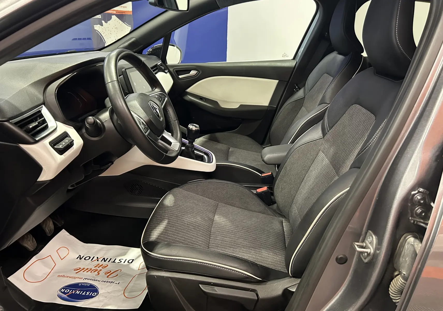 Intérieur avant droit d'une Renault Clio V gris 2023, sièges tissu et cuir avec volant multifonction et boîte manuelle.