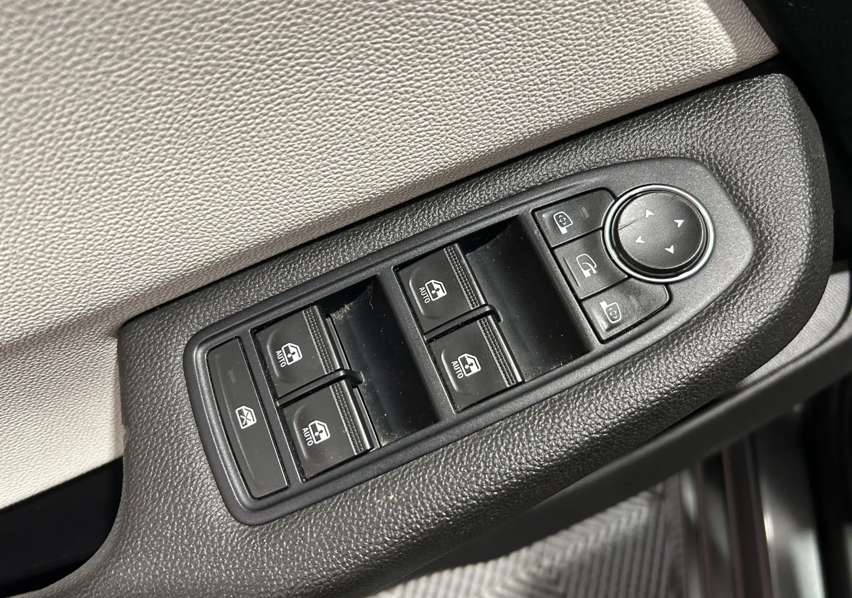Gros plan sur les commandes des vitres électriques et rétroviseurs côté conducteur d'une Renault Clio V gris 2023.
