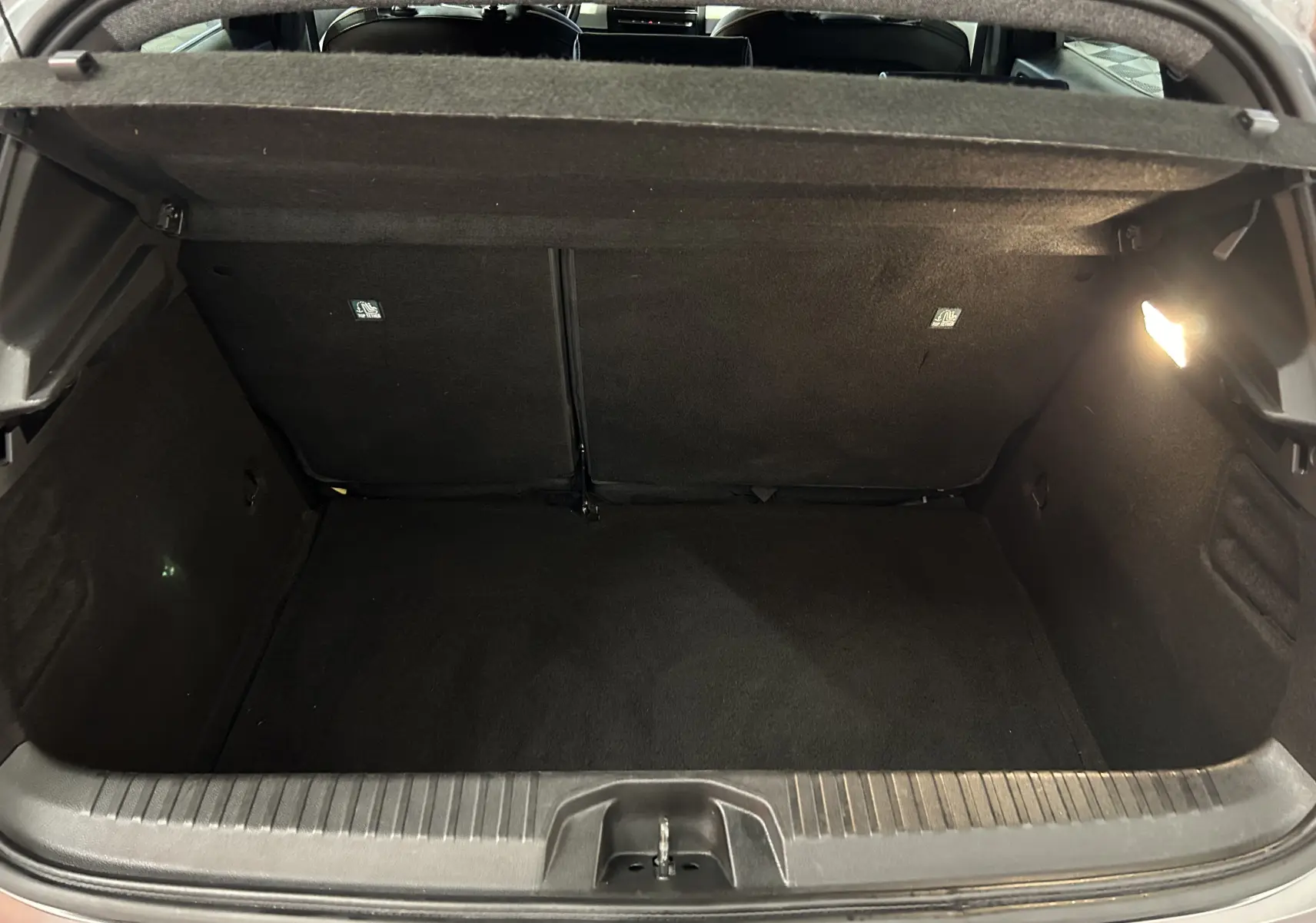 Coffre ouvert de la Renault Clio V TCe 90 TECHNO gris, vue intérieure arrière montrant l'espace de chargement vide et éclairé.