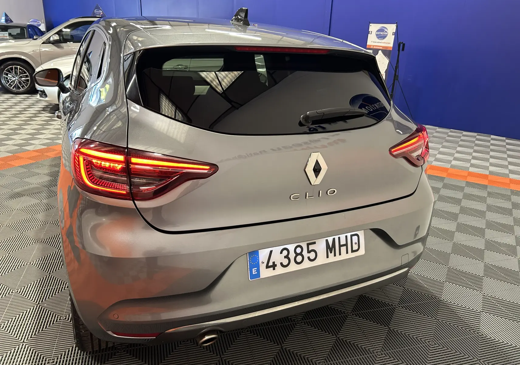 Vue arrière droite d'une Renault Clio V gris métallisé 2023 avec feux allumés dans un showroom.