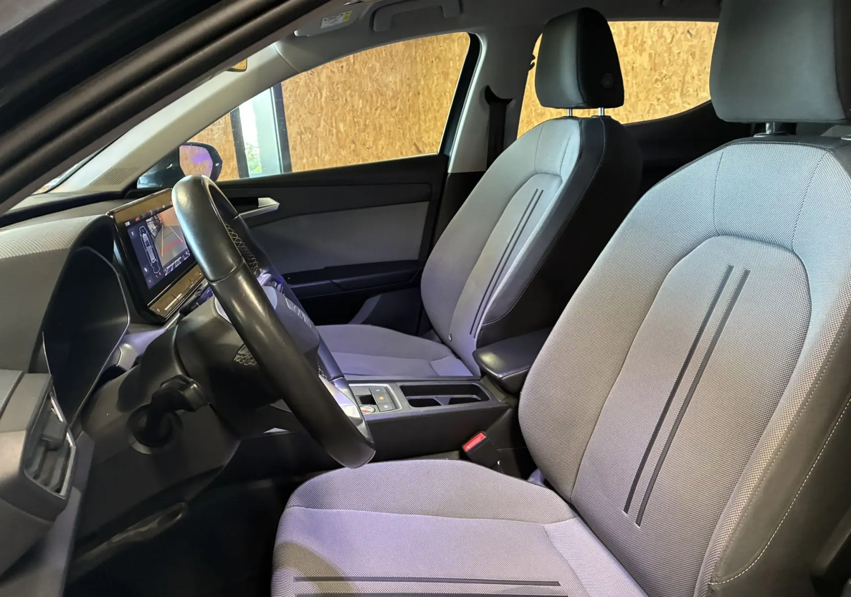 Vue intérieure côté conducteur de la SEAT Leon 2.0 TDI 115 STYLE 2021, sièges tissu gris avec volant noir et écran tactile.