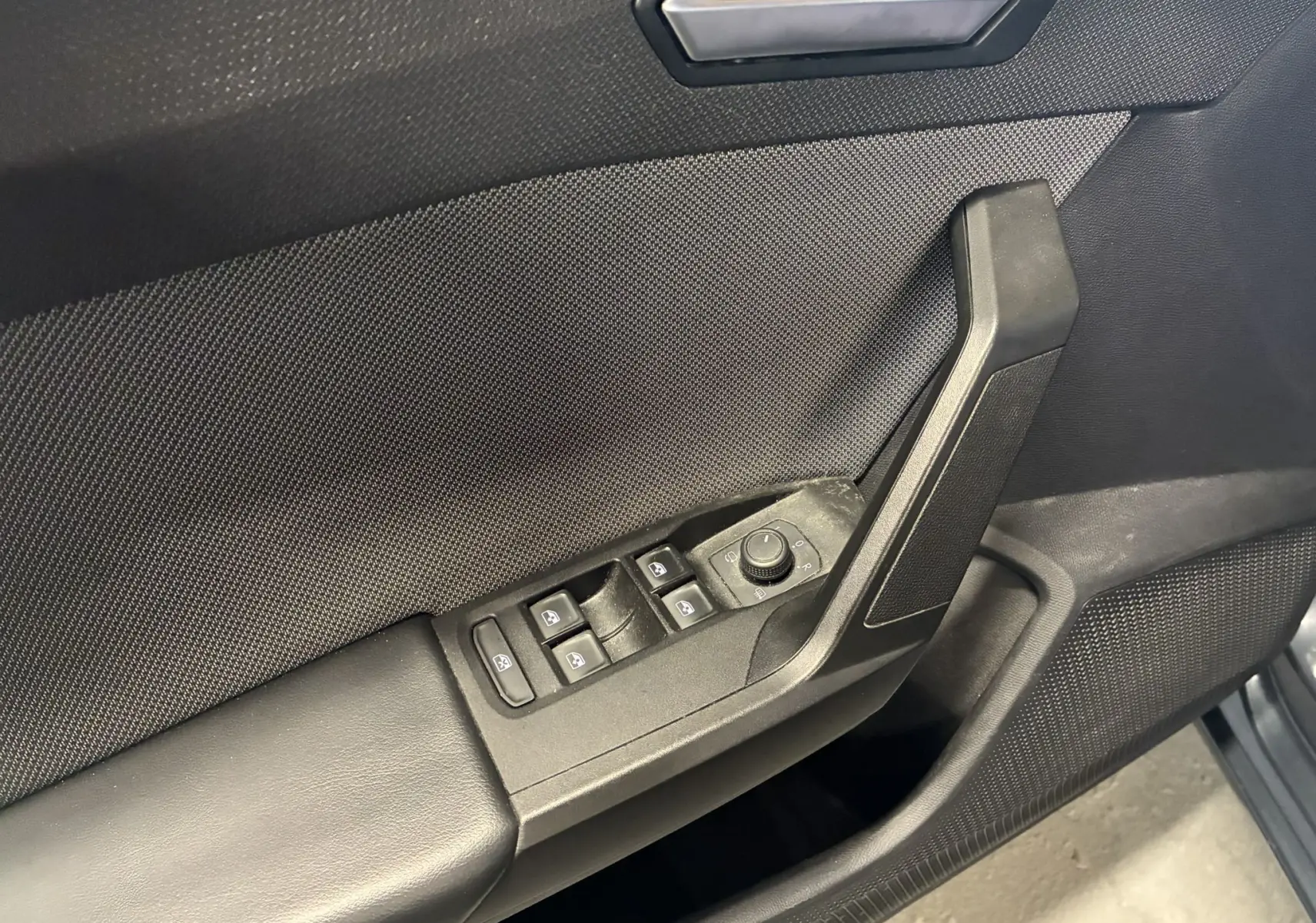 Gros plan sur la commande des vitres et rétroviseurs côté conducteur d'une SEAT LEON gris 2021, intérieur noir.
