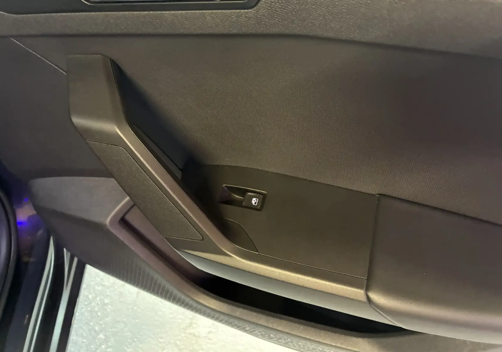 Détail de la porte intérieure côté conducteur d'une SEAT Leon gris 2021, avec bouton de commande de vitre électrique.