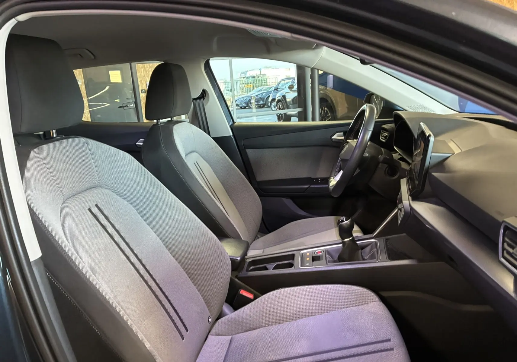 Intérieur de la SEAT LEON 2.0 TDI 115 STYLE 2021, vue côté conducteur montrant sièges gris tissu et tableau de bord noir.