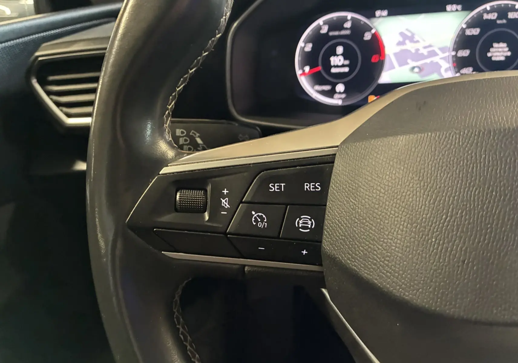 Gros plan sur le côté gauche du volant noir du SEAT LEON 2021, avec commandes de régulateur et tableau de bord numérique en arrière-plan.