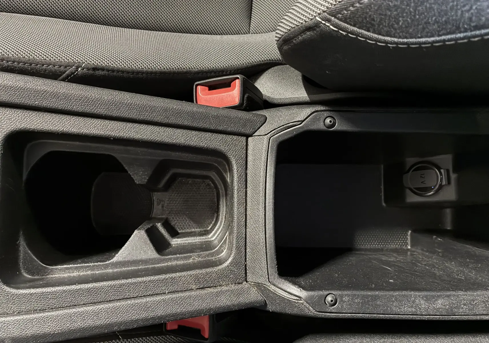 Gros plan intérieur sur la console centrale noire du SEAT LEON 2.0 TDI 115 STYLE avec porte-gobelets et prise 12V.