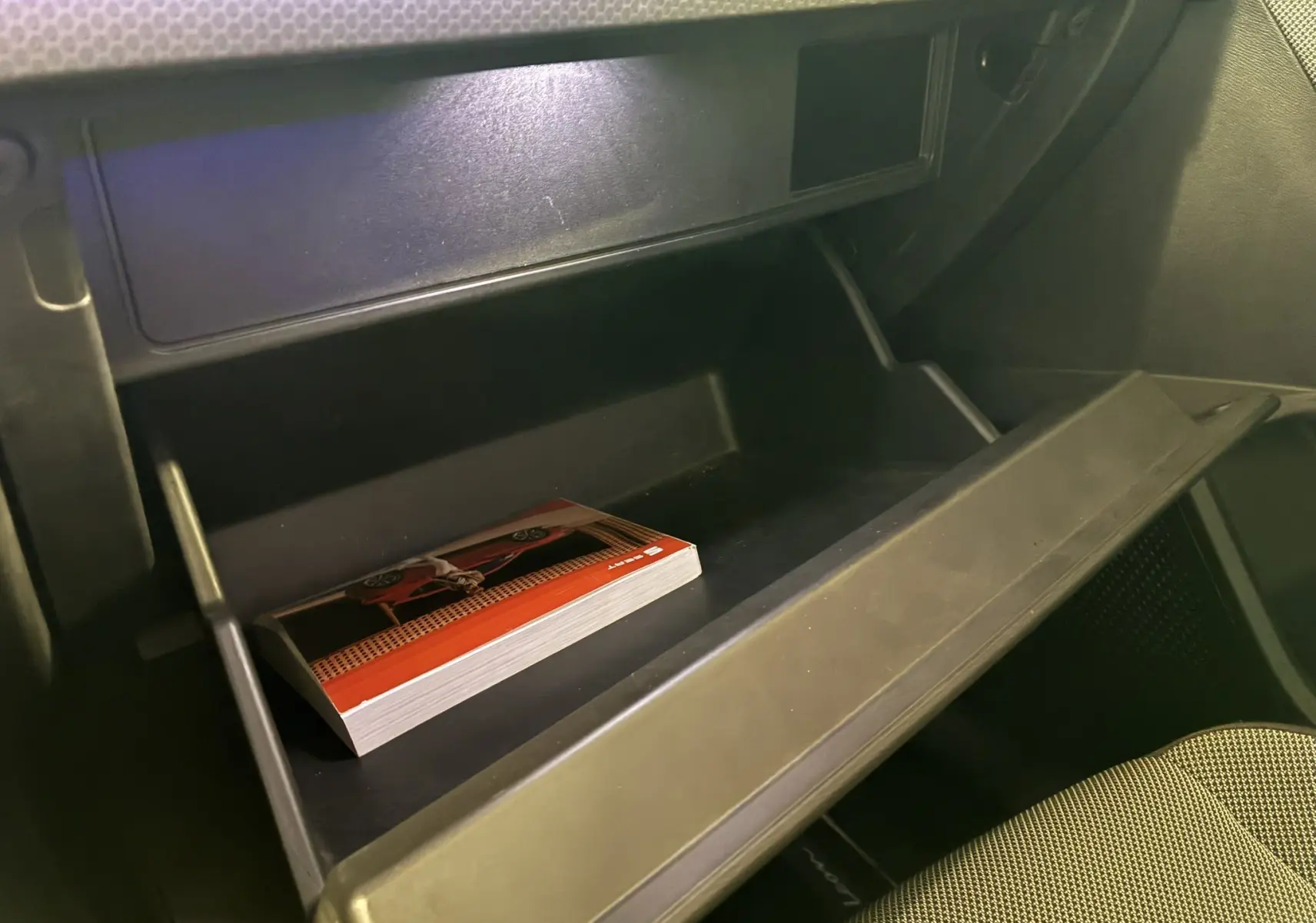 Gros plan sur la boîte à gants ouverte côté passager d'une SEAT Leon gris 2021 avec un manuel à l'intérieur.