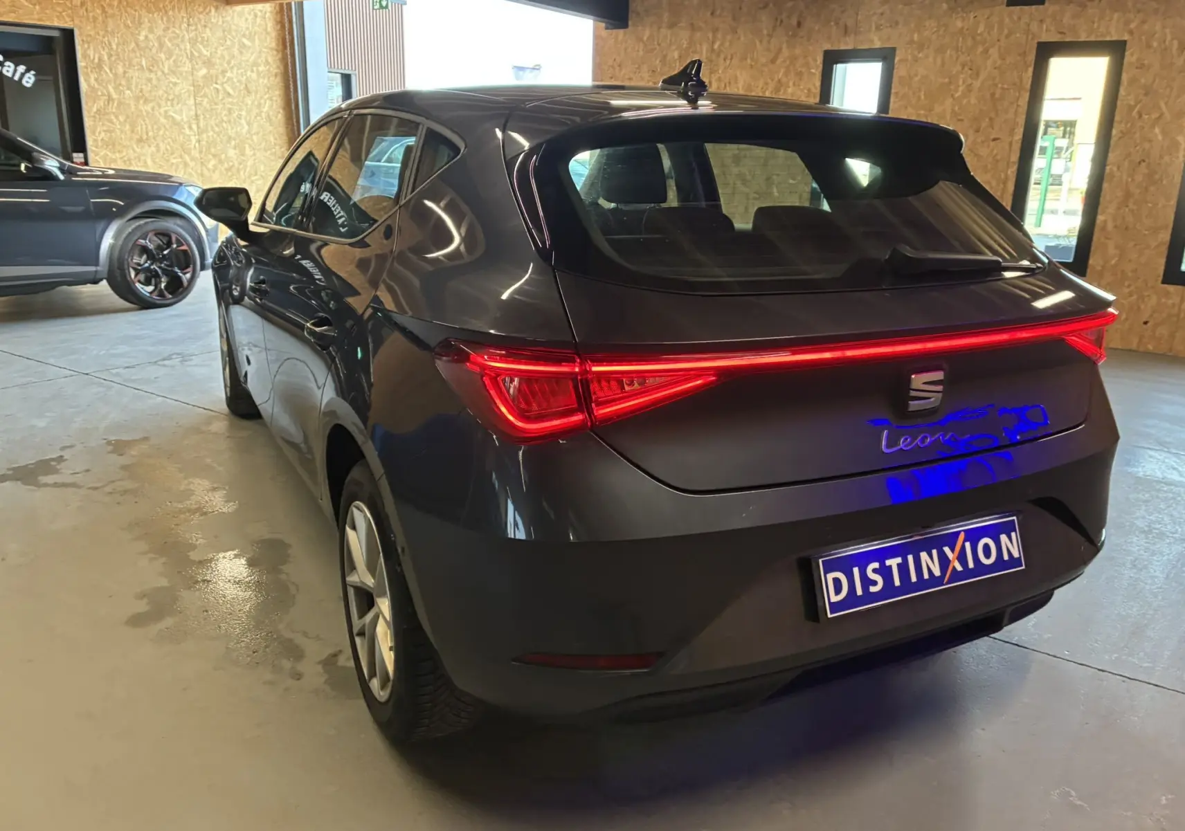 Vue 3/4 arrière droite d'une SEAT Leon gris métallisé 2021 avec feux arrière allumés dans un garage.