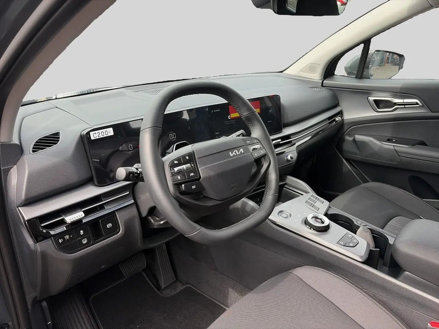 Intérieur avant du Kia Sportage 1.6 hybride 2026, vue côté conducteur, tableau de bord et volant cuir multifonction.