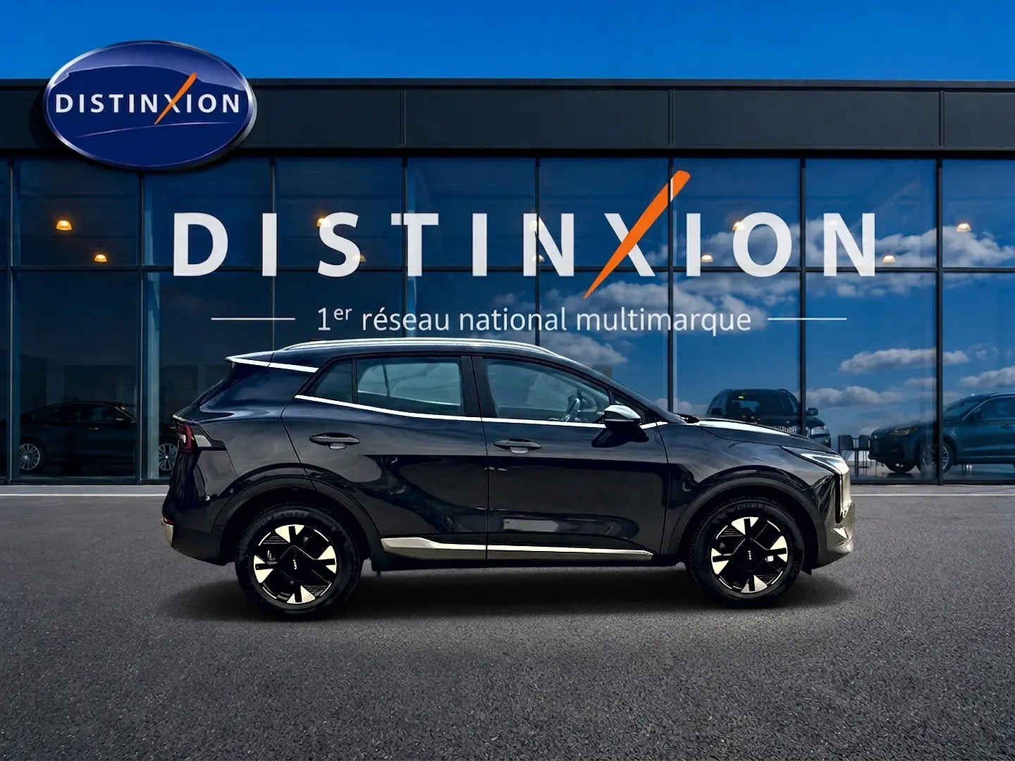 Profil côté gauche du KIA SPORTAGE 1.6 hybride 239 active gris eclipse avec jantes alu noires devant une vitrine Distinxion.