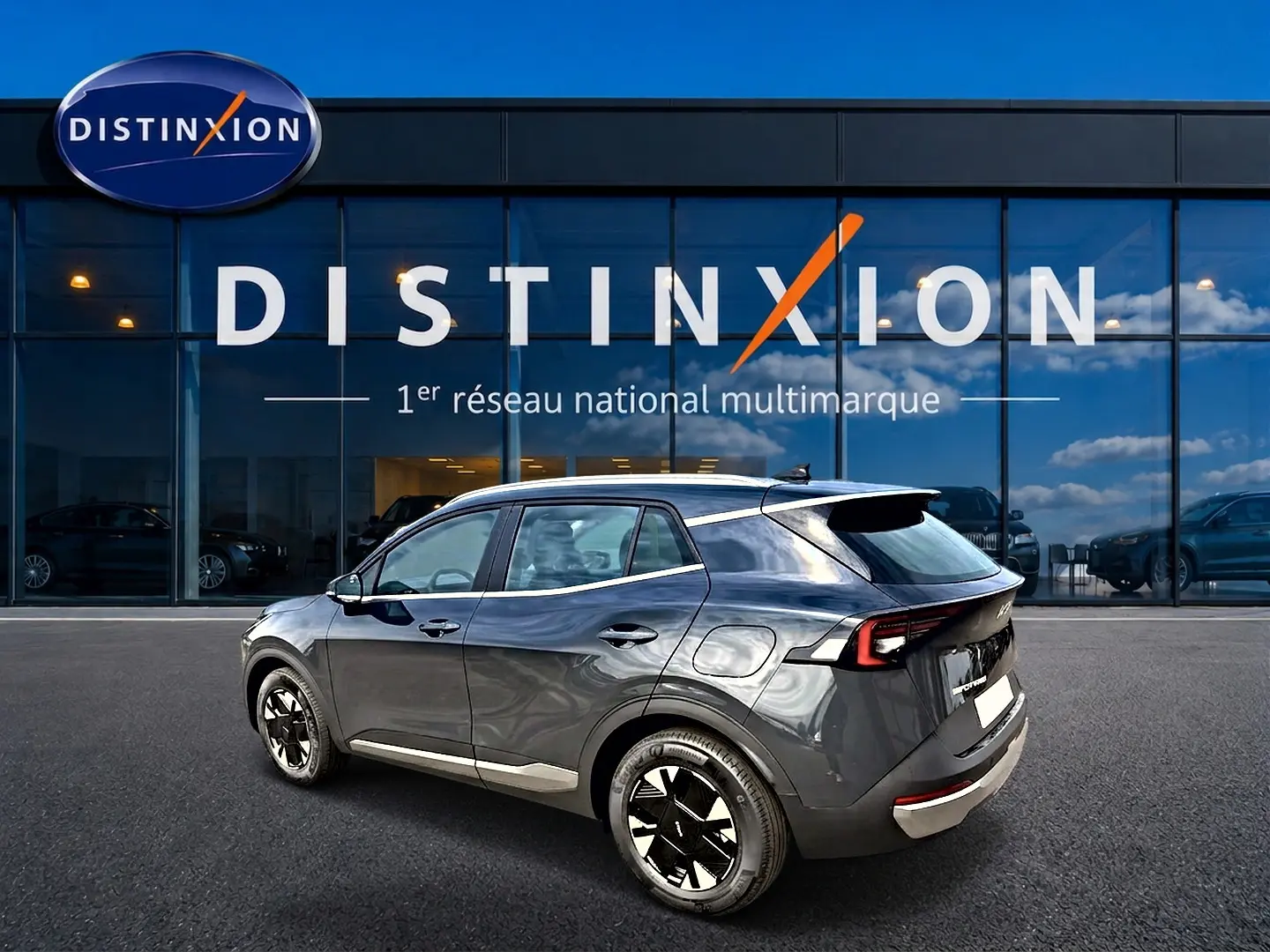 Vue 3/4 arrière droite du KIA SPORTAGE 1.6 hybride gris eclipse avec jantes alu et feux arrière LED, devant un showroom Distinxion.