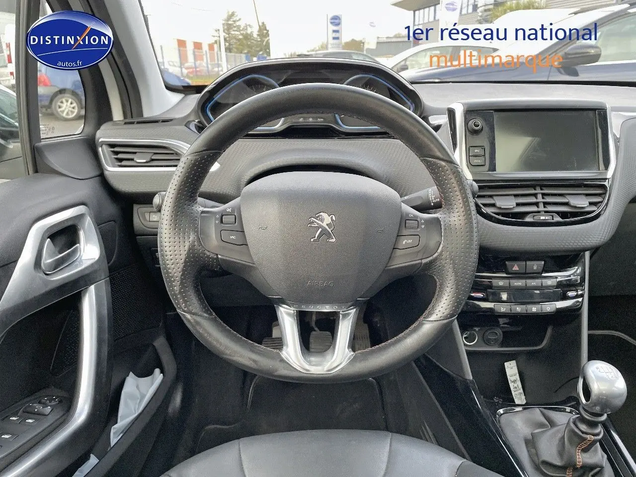 Vue intérieure centrée sur le volant cuir noir et la console centrale d'une Peugeot 2008 blanche de 2016 avec boîte manuelle.