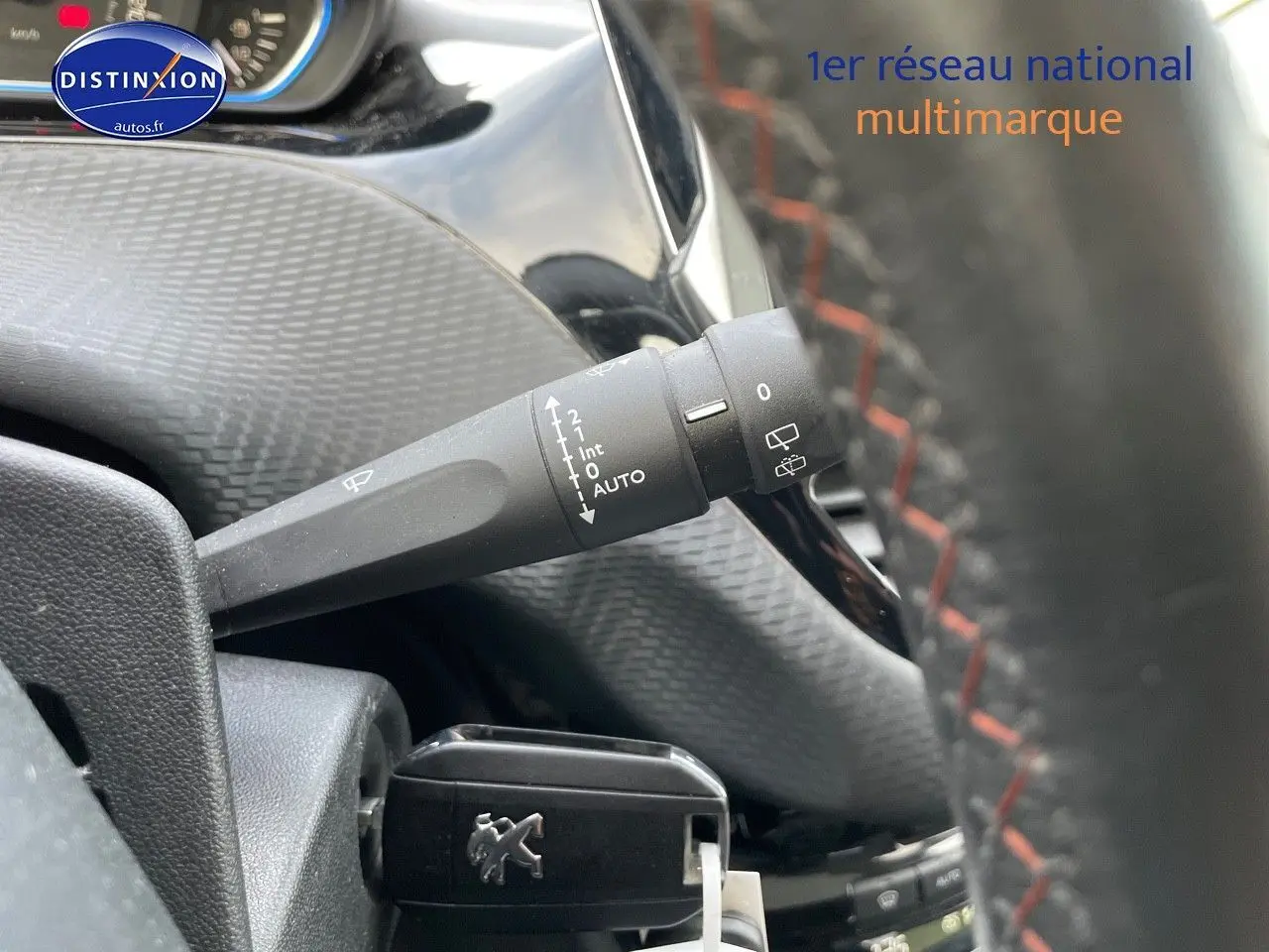 Gros plan sur la commande d’essuie-glace à gauche du volant d’un Peugeot 2008 blanc, intérieur noir avec surpiqûres rouges.