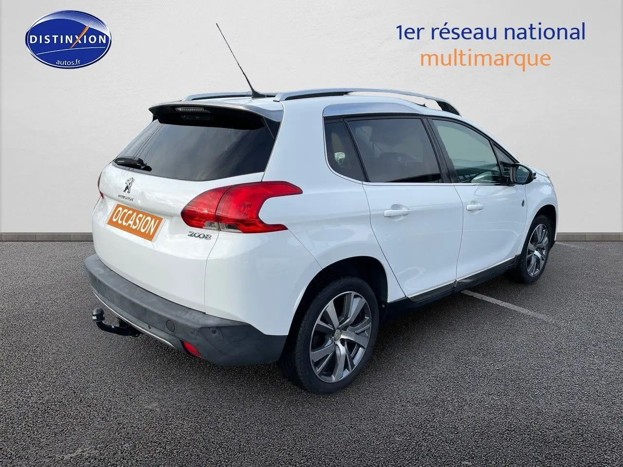 Peugeot 2008 blanc en 3/4 arrière droit, avec barres de toit et attelage visible sur parking.