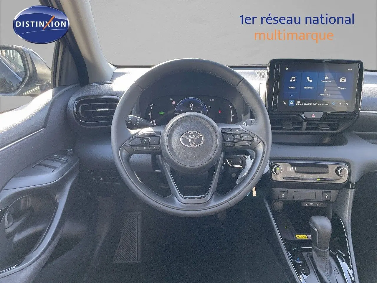 Vue intérieure frontale du poste de conduite de la Toyota Yaris Hybrid 116ch 2025 avec écran tactile et volant multifonction noir.