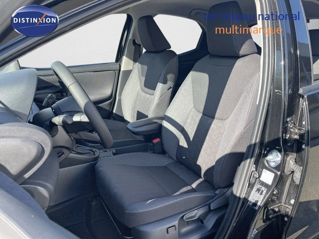 Vue intérieure côté conducteur de la Toyota Yaris Hybrid 2025 noir métal, sièges tissu gris et volant visible.