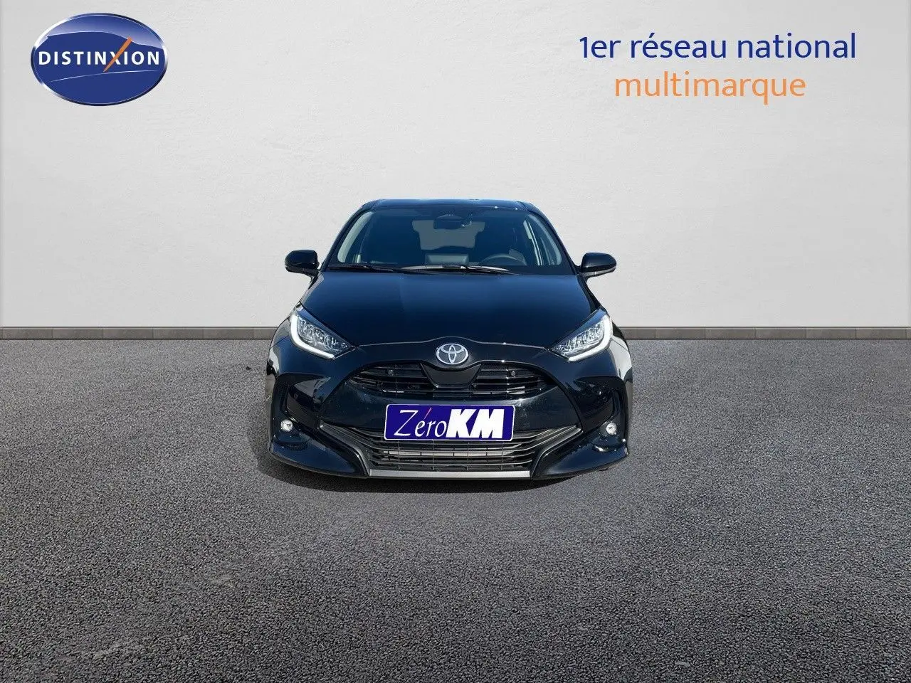 Vue frontale d'une Toyota Yaris Hybrid 116ch noir métal avec calandre imposante et phares LED allumés.