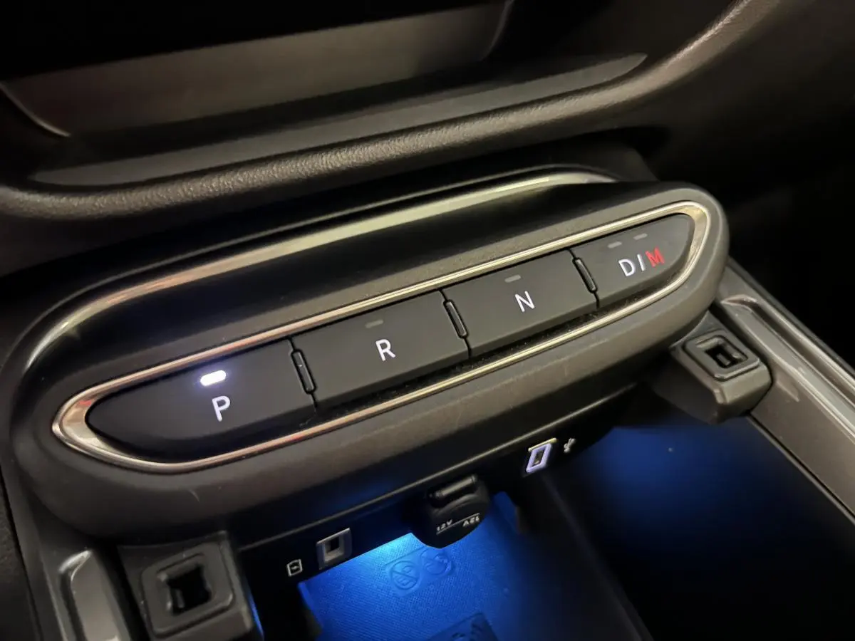 Gros plan sur la console centrale noire de la Fiat 600 Hybrid 2024 avec boutons de boîte auto éclairés et éclairage bleu dessous.
