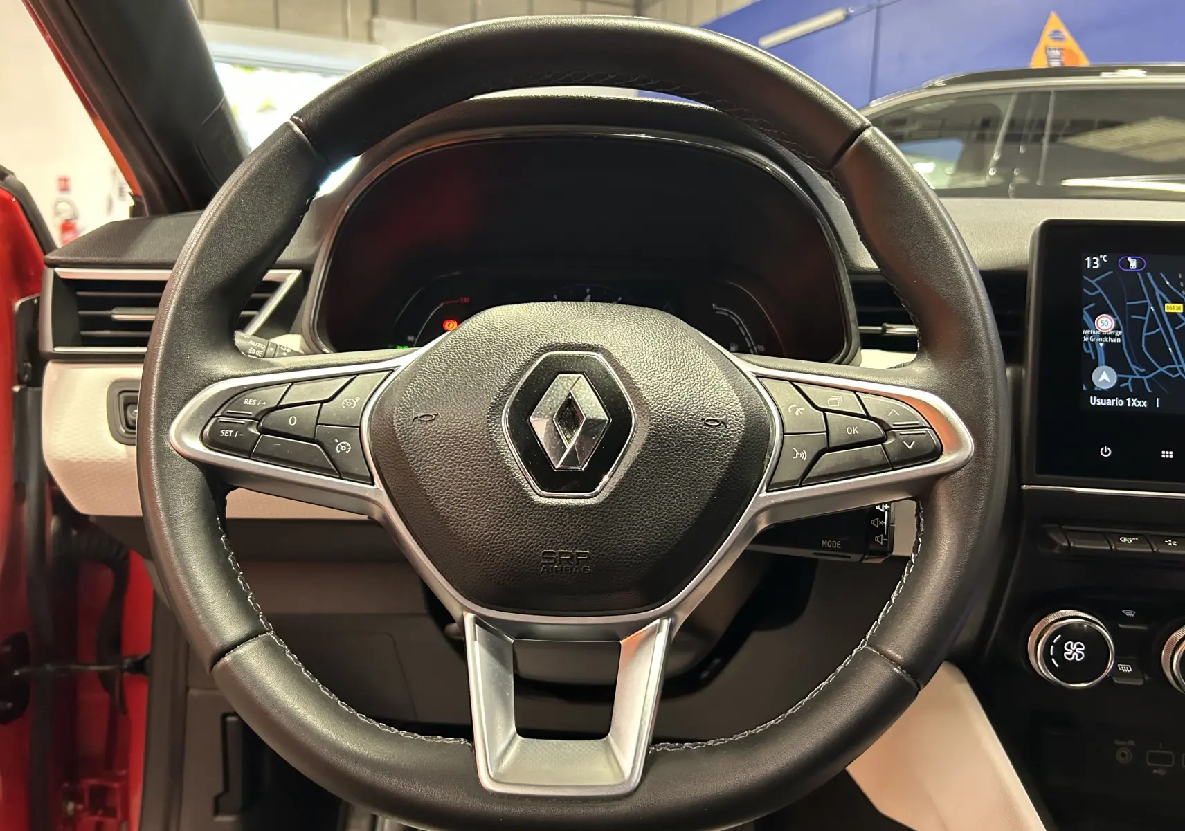 Vue rapprochée du volant cuir noir avec commandes intégrées de la Renault Clio V TCe 90 rouge, tableau de bord et écran tactile visibles.