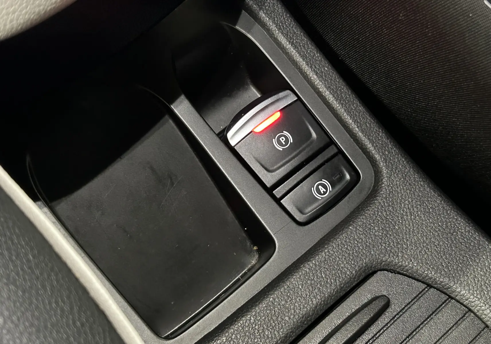 Gros plan sur les commandes de frein à main électronique et d'assistance au démarrage en côte dans l'habitacle noir d'une Renault Clio V rouge.