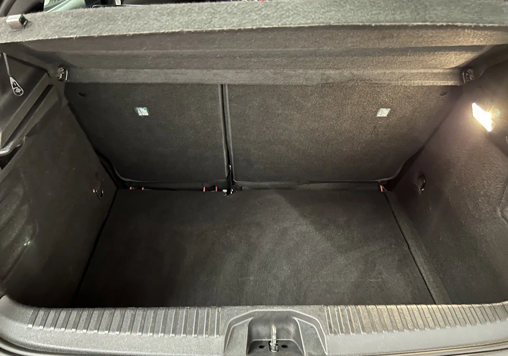 Coffre ouvert vu de l'arrière d'une Renault Clio V TCe 90 TECHNO rouge, intérieur noir avec éclairage à droite.