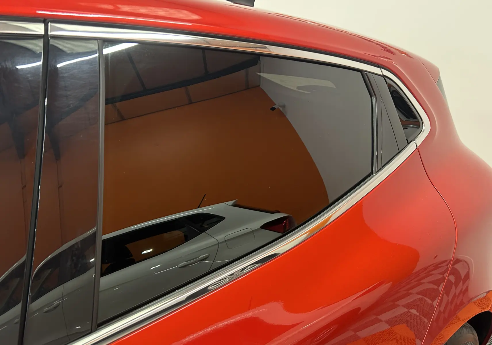 Gros plan sur la partie arrière droite d'une Renault Clio V rouge 2023 avec vitres teintées et contours chromés.