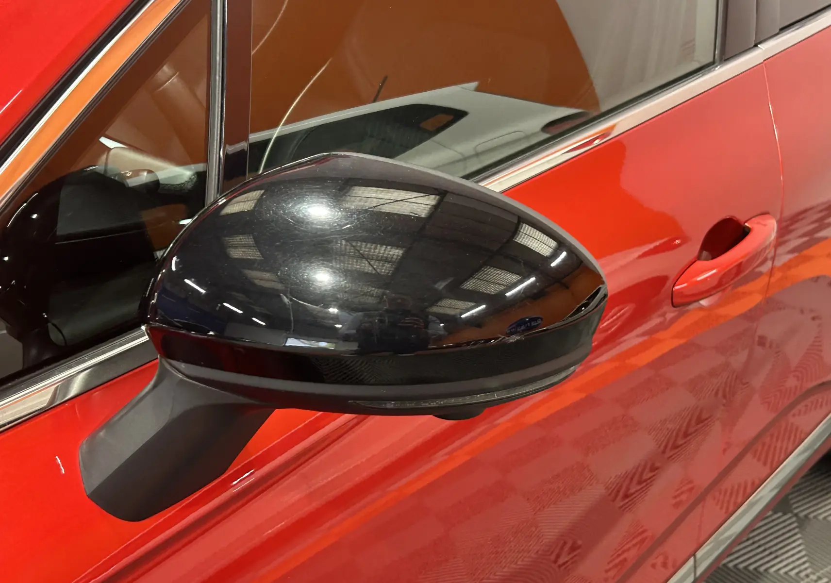 Gros plan sur le rétroviseur noir côté gauche d'une Renault Clio V rouge 2023 avec caméra 360° intégrée.