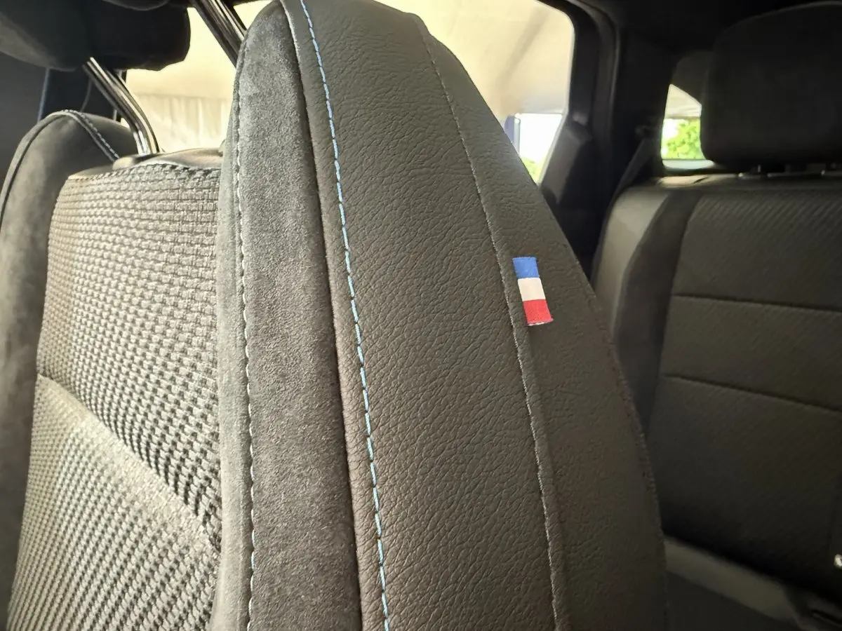Gros plan sur le dossier avant gauche en cuir noir avec surpiqûres bleues et drapeau tricolore du Renault Espace esprit Alpine 2025.