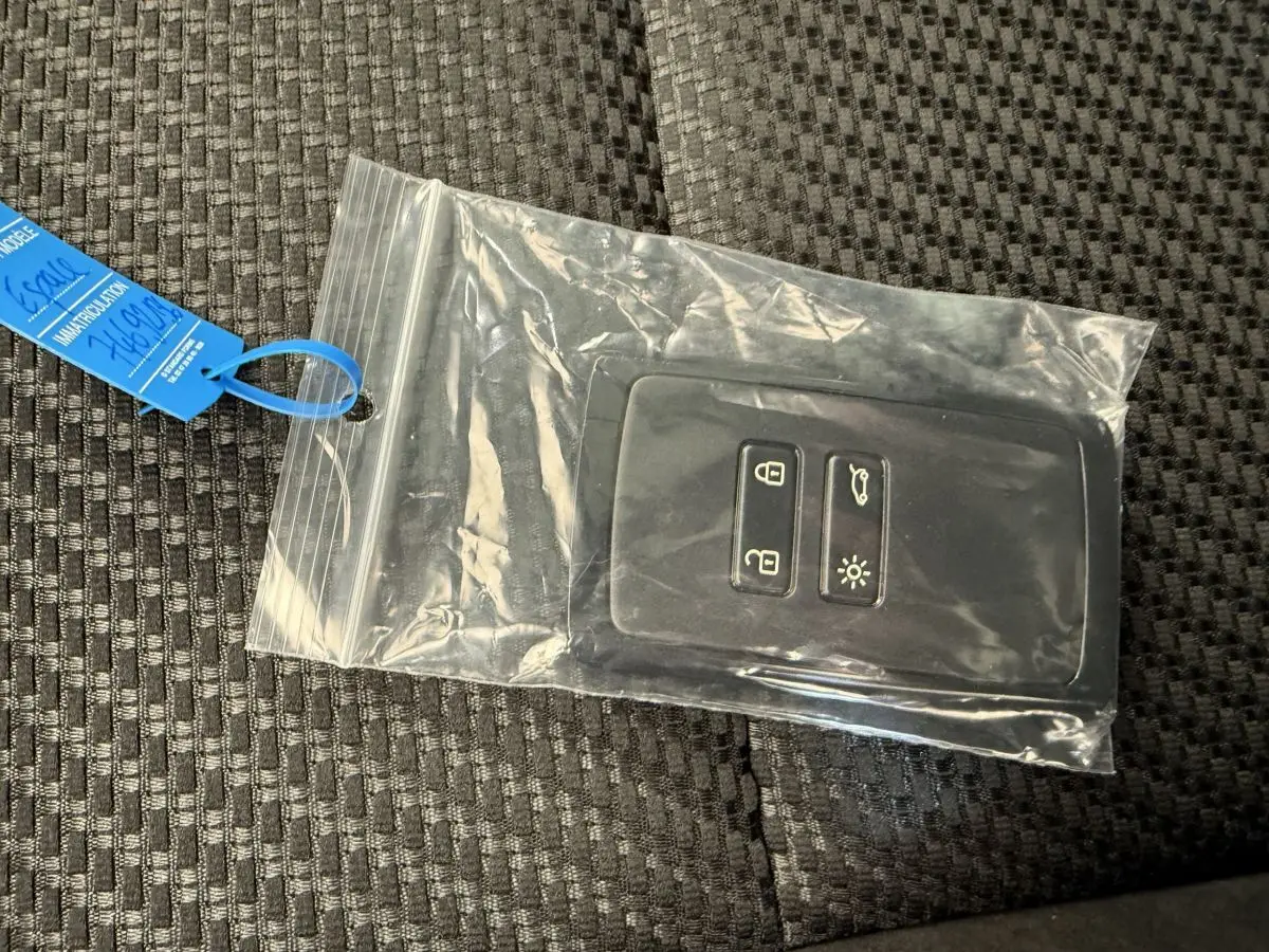 Télécommande noire Renault Espace esprit Alpine 7 places dans pochette plastique sur tissu gris foncé.