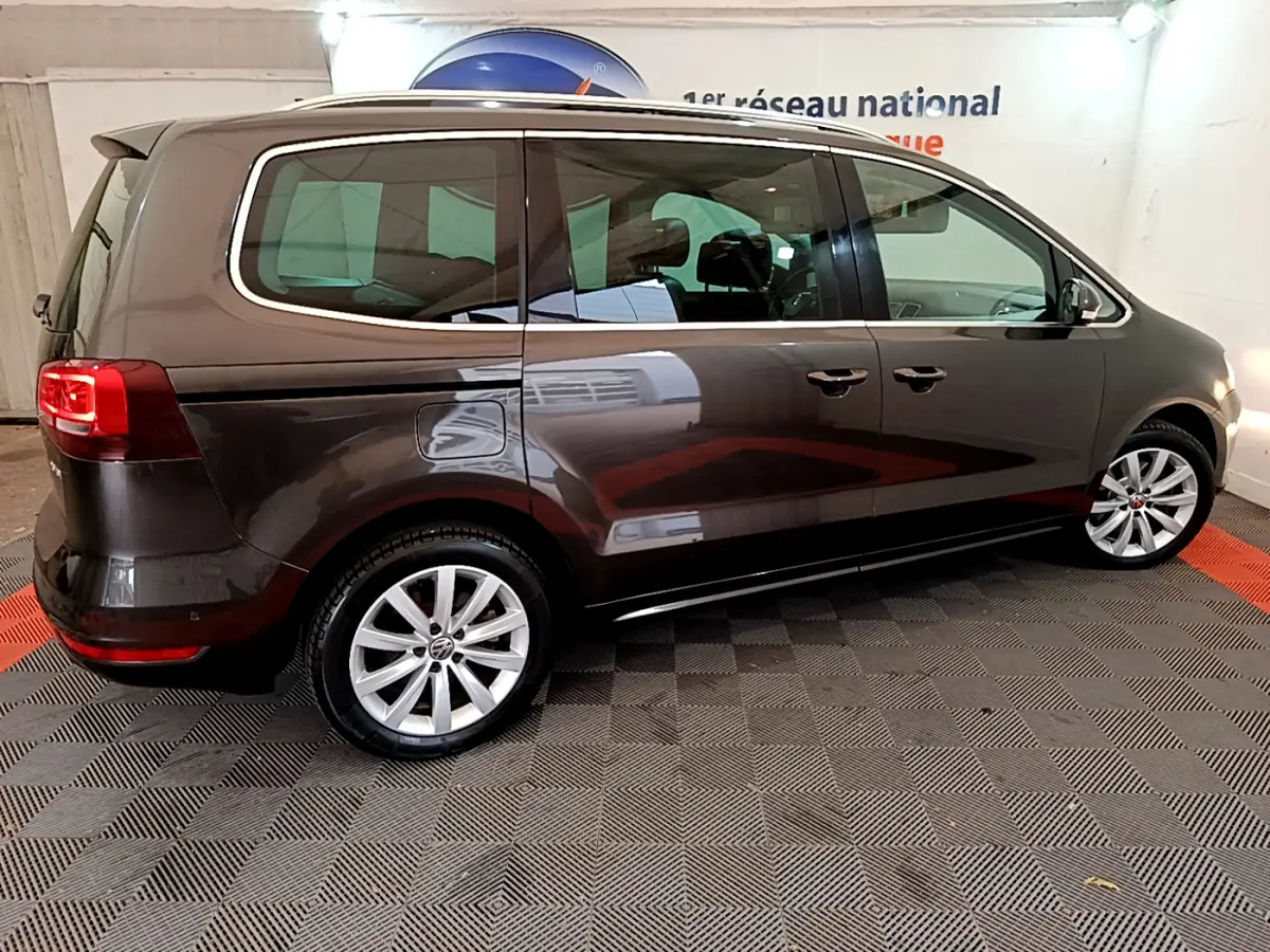Vue de profil côté gauche d'un Volkswagen Sharan marron 2017 sur sol damier intérieur showroom.